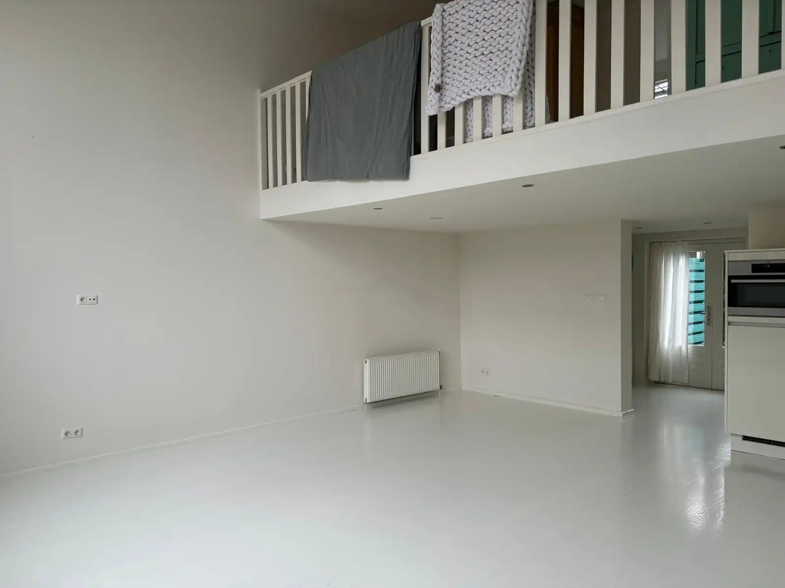 Lichte woonruimte met vide en wit hekwerk, muren en plafond strak wit opgeleverd.