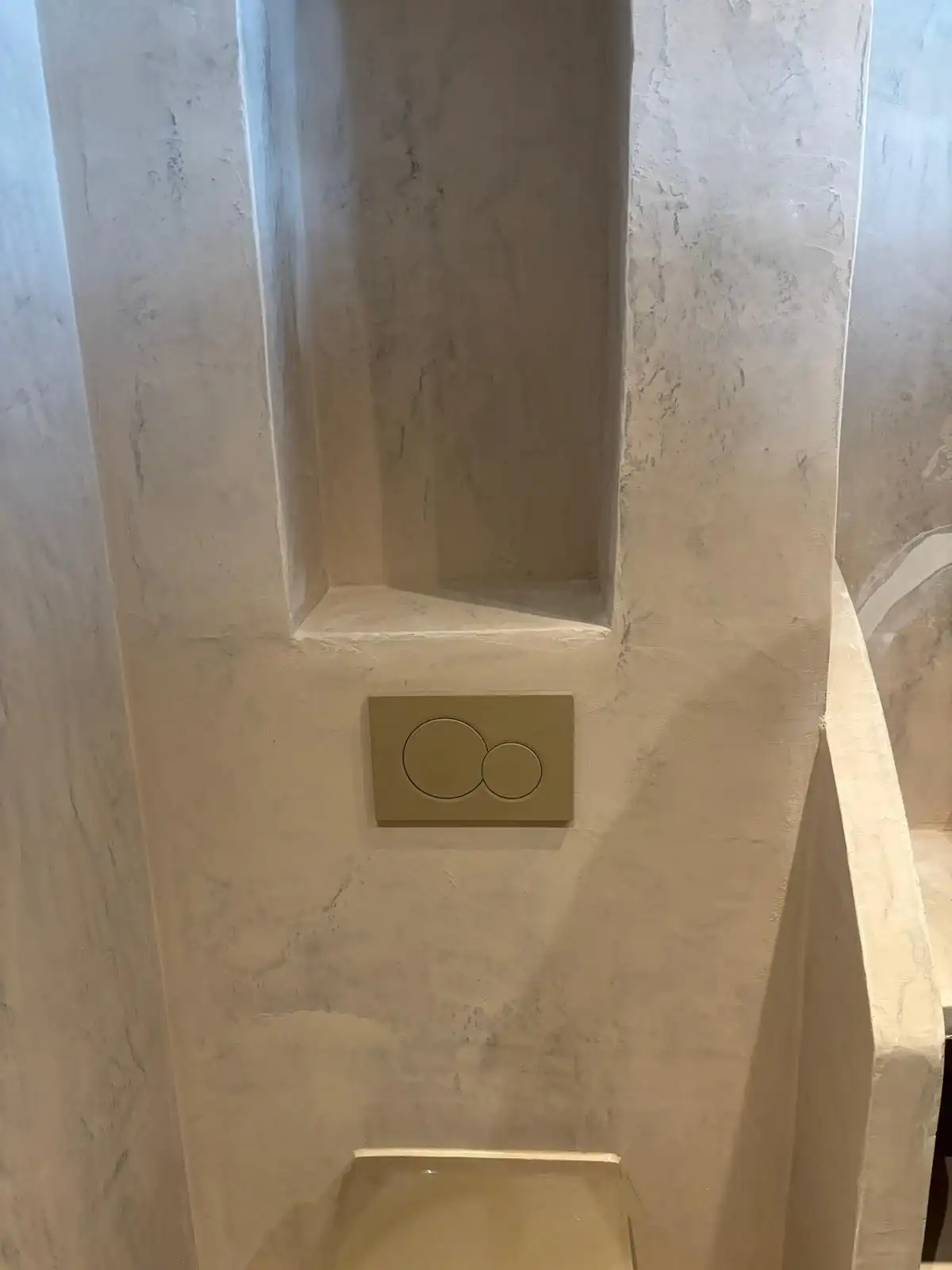 Toiletruimte met nis en spoelknop, afgewerkt in sierpleister.