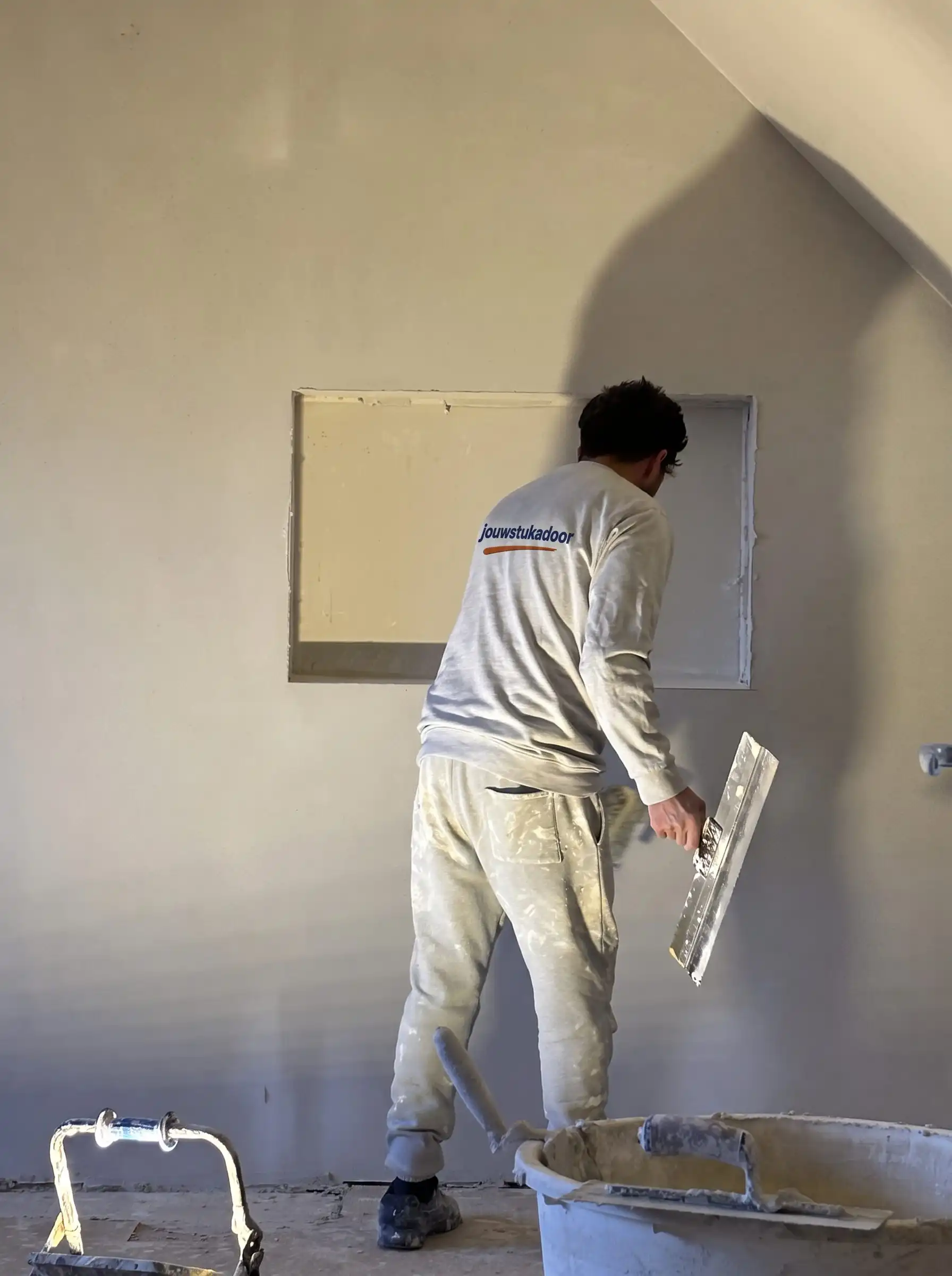Stukadoor van jouwstukadoor zet met de spaan een nis af, in laag zonlicht.